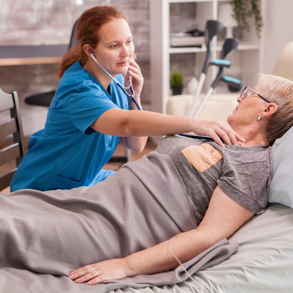 Female doctor using stethoscope to check old woman heart in nursing home.